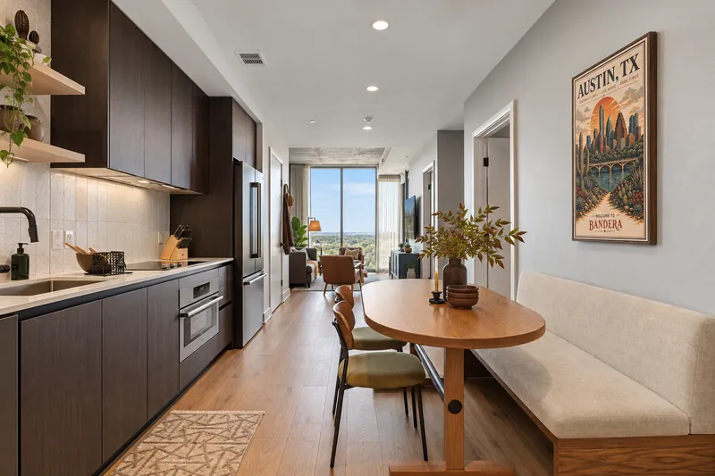 Galley kitchen with dark cabinetry opening to an oval dining table and bench seating