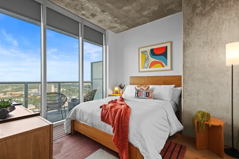 Bedroom with a made bed and abstract art, with a balcony visible through floor-to-ceiling glass