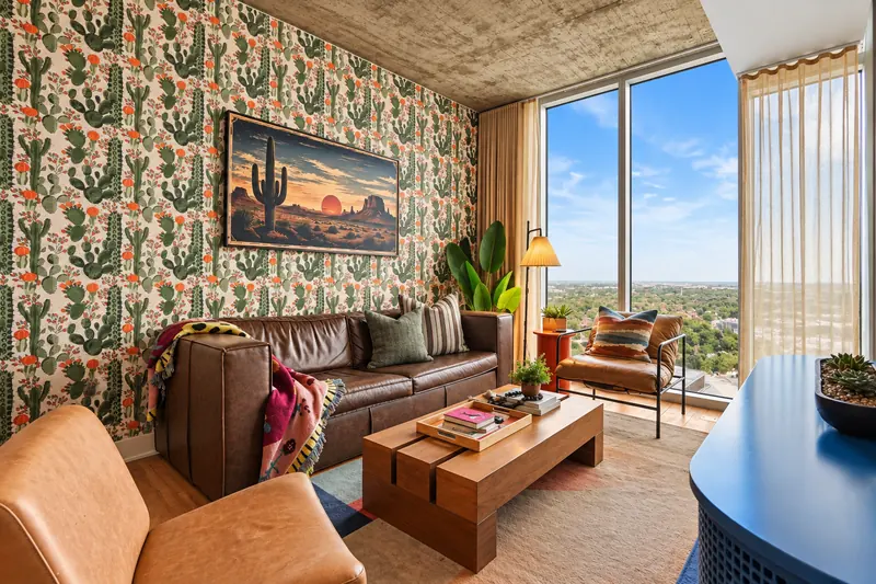 Living area with cactus wallpaper, desert artwork, leather sofa and a window view over the city