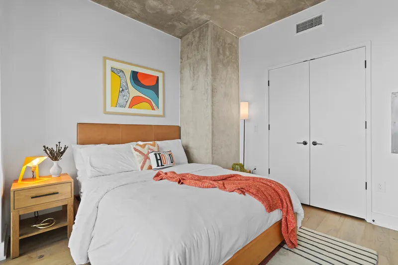 Bedroom with white bedding, wood headboard, bedside lamp and abstract art above the bed
