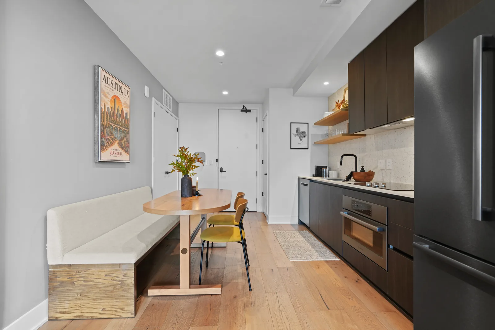 Oval wood dining table with bench seating and an Austin poster, kitchen and entry beyond