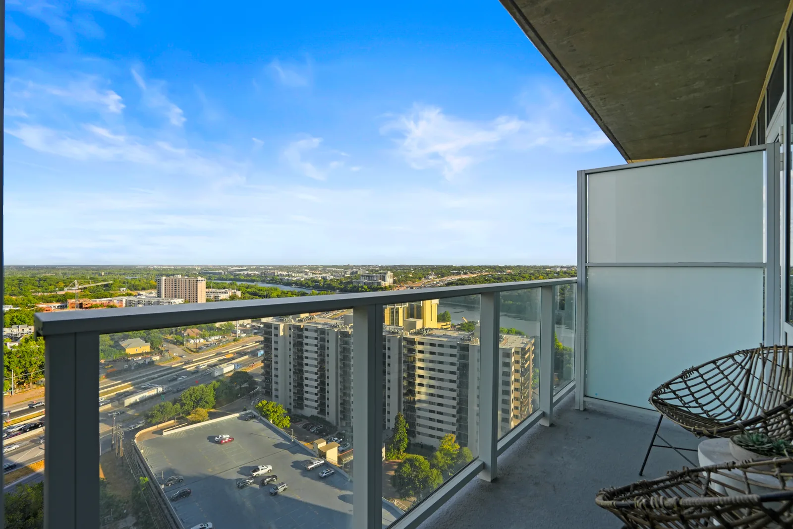 Private balcony with glass railing and woven chairs overlooking the city