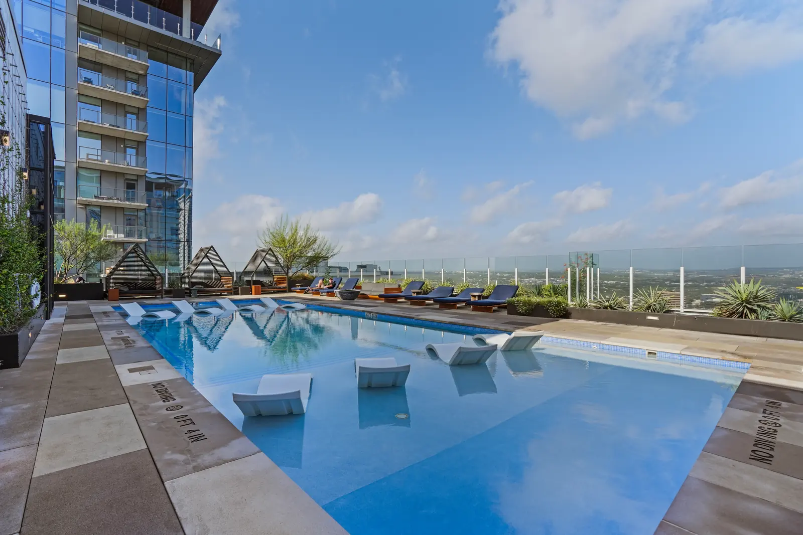 Shared rooftop pool with in-pool loungers and a lounge deck under open sky, with a guest relaxing on a lounge chair