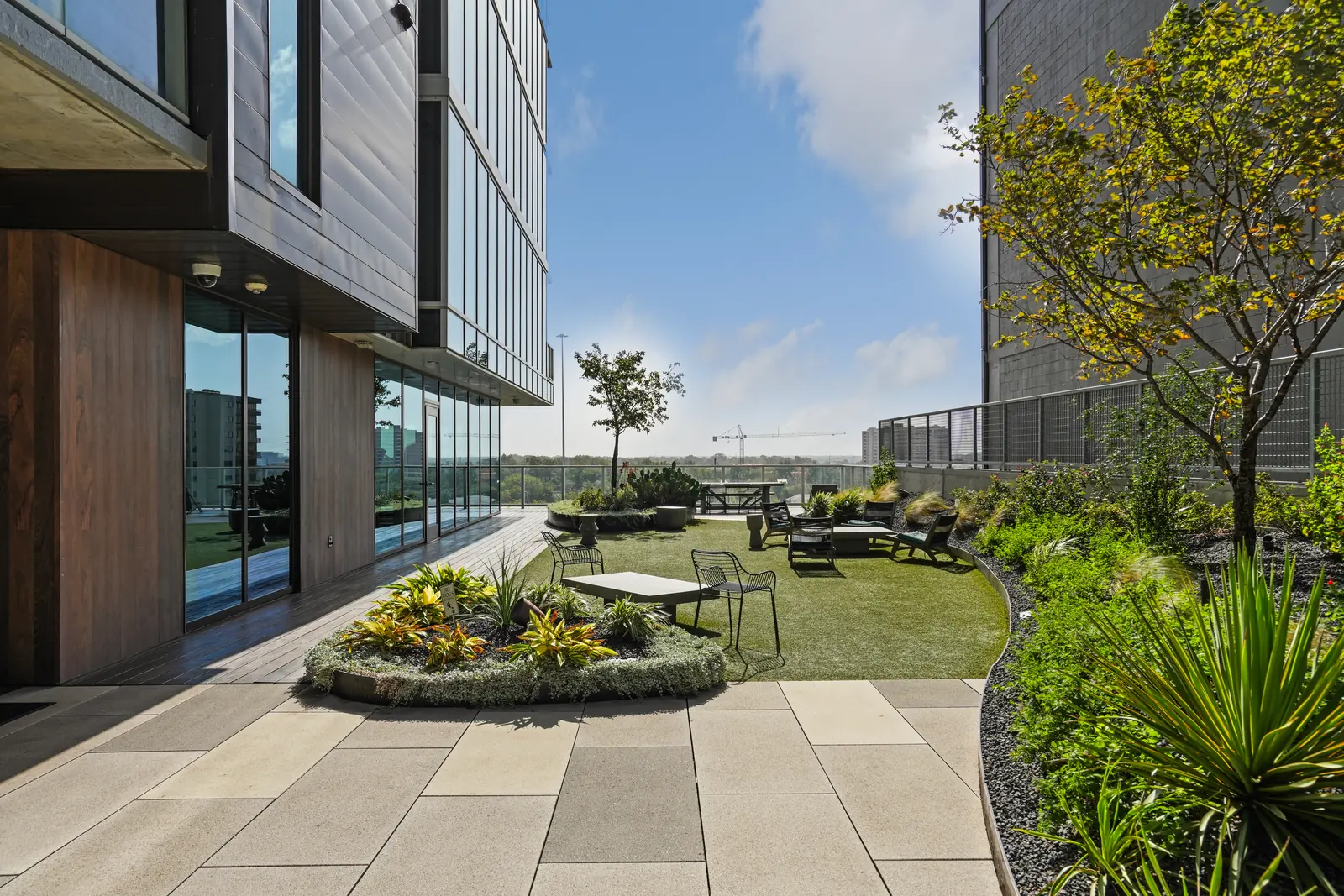 Shared outdoor terrace with a turf lawn, a round planter, patio tables and landscaped beds beside the building