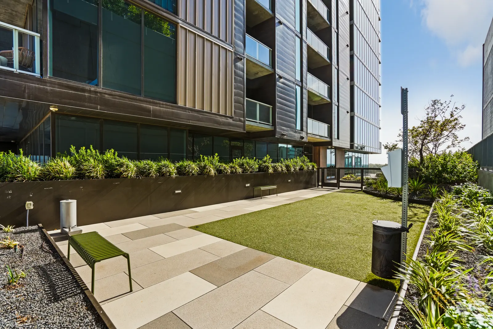 Shared terrace with a turf lawn, paved walkway, planting beds and a bench along the building