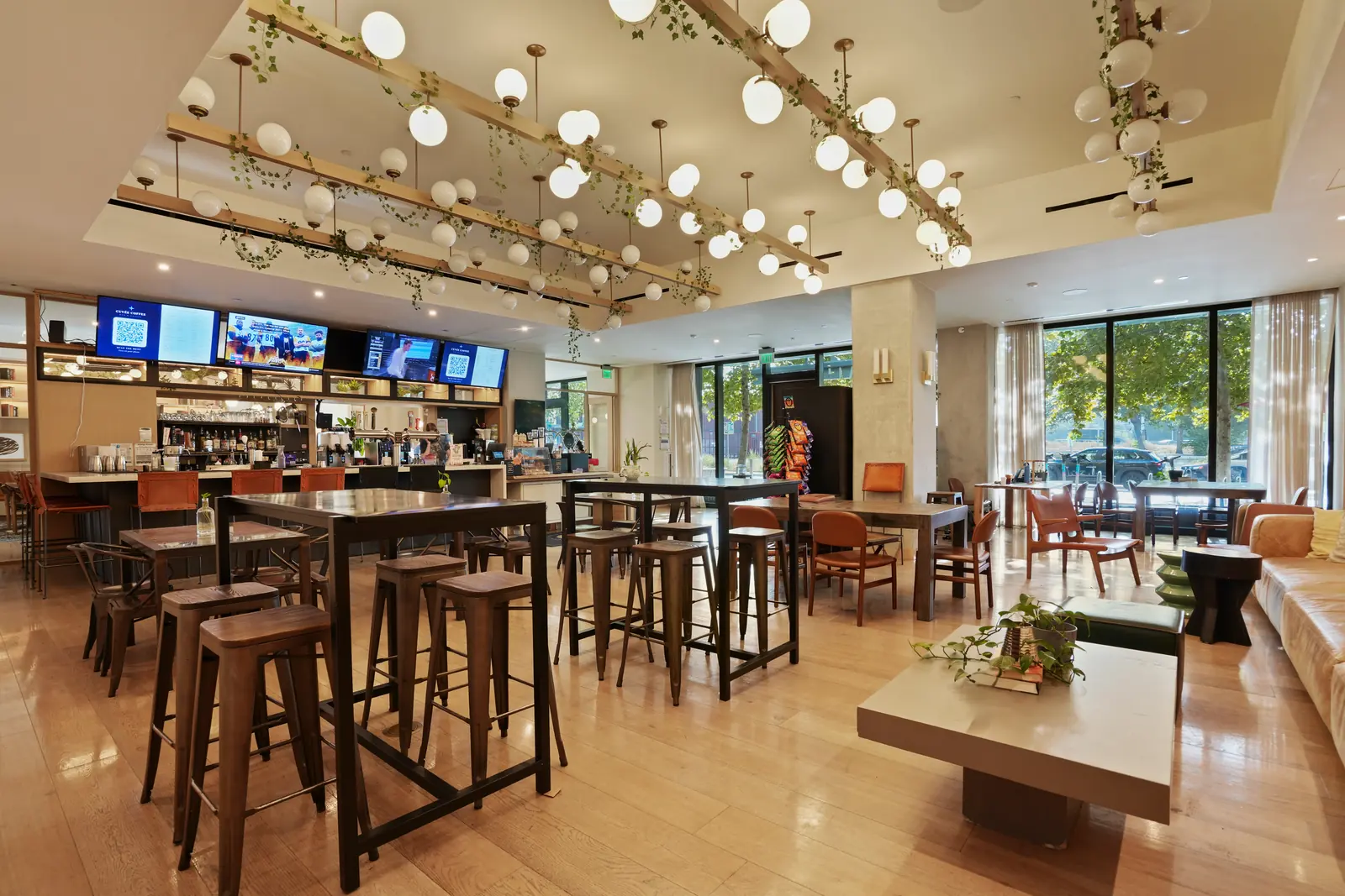 Ground-floor café and bar with high-top tables, stools, wall-mounted TVs and a staff member behind the counter