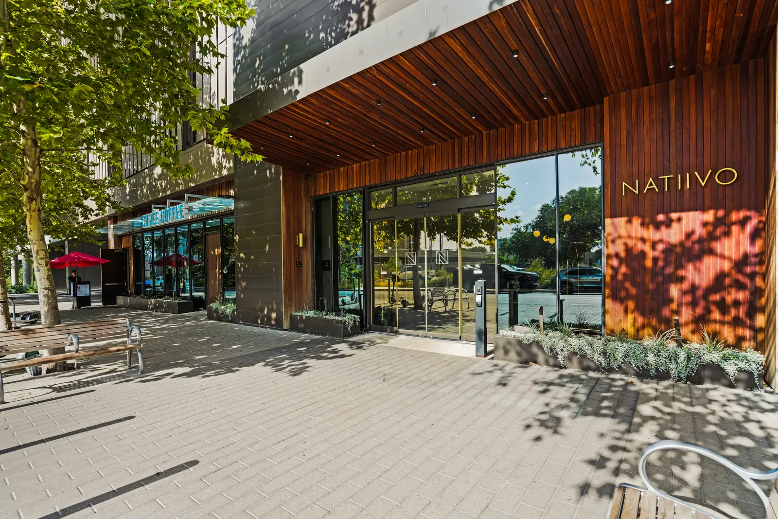 Natiivo street entrance with wood-clad walls, glass doors, the Natiivo sign and café seating under a red umbrella